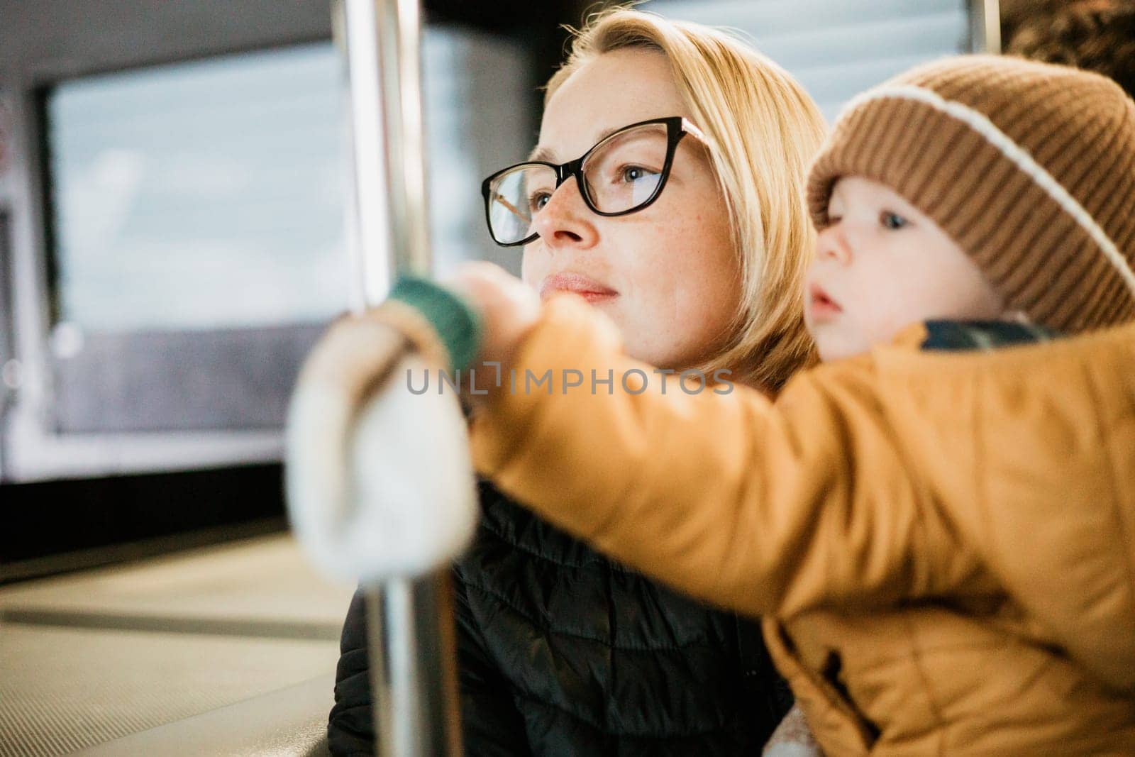 Mother carries her child while standing and holding on to the bus. Mom holding her infant baby boy in her arms while riding in a public transportation. Cute toddler boy traveling with his mother