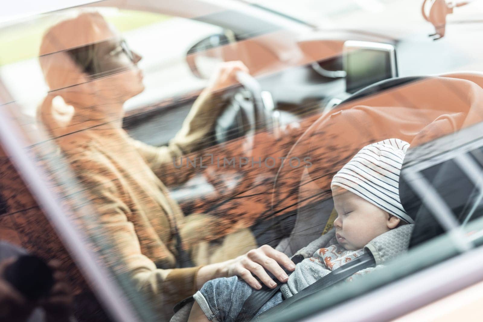 Mother concentrating on driving family car running errands while her baby sleeps in infant car seat by her site