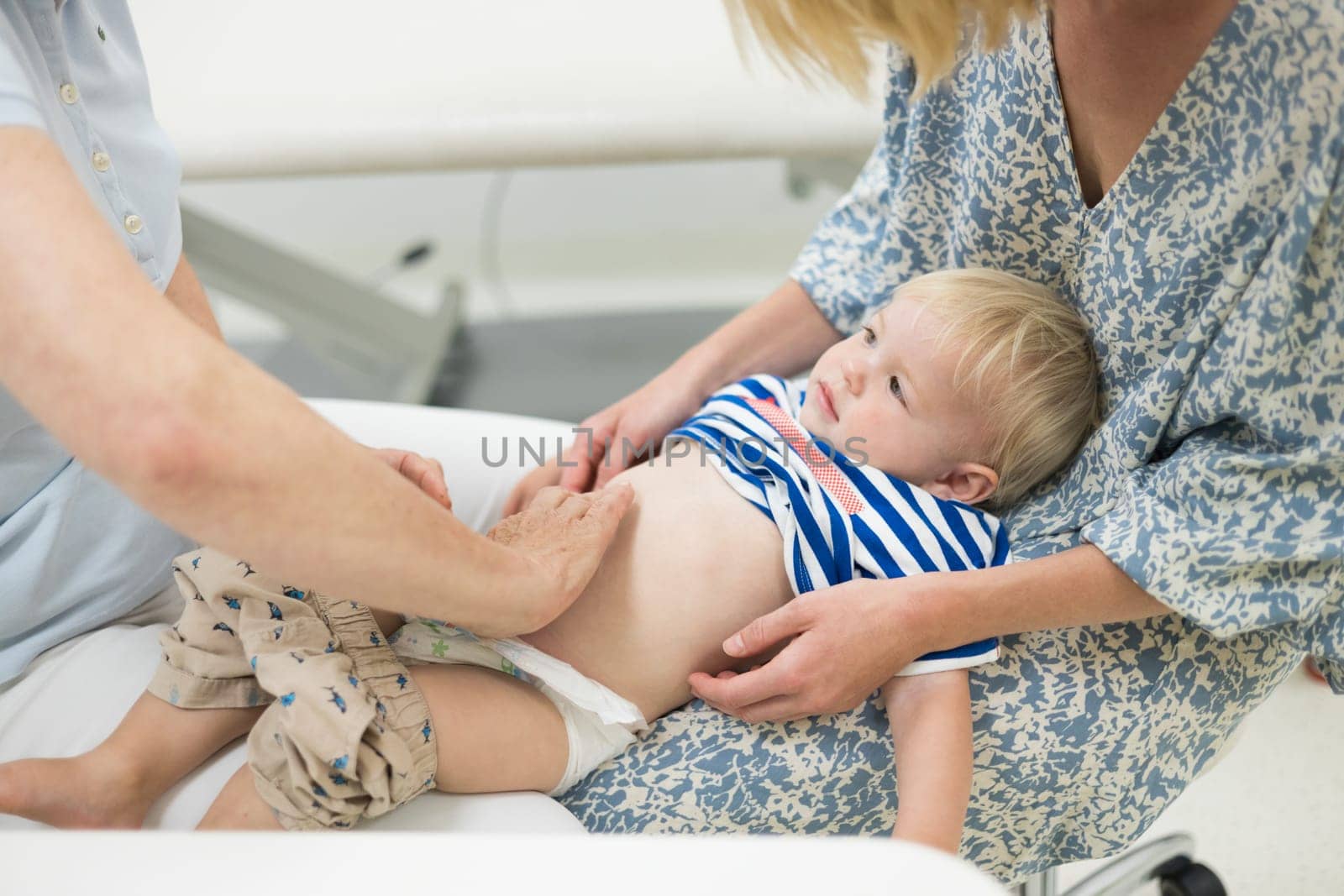 Infant baby boy child being examined by his pediatrician doctor during a standard medical checkup in presence and comfort of his mother. National public health and childs care care koncept