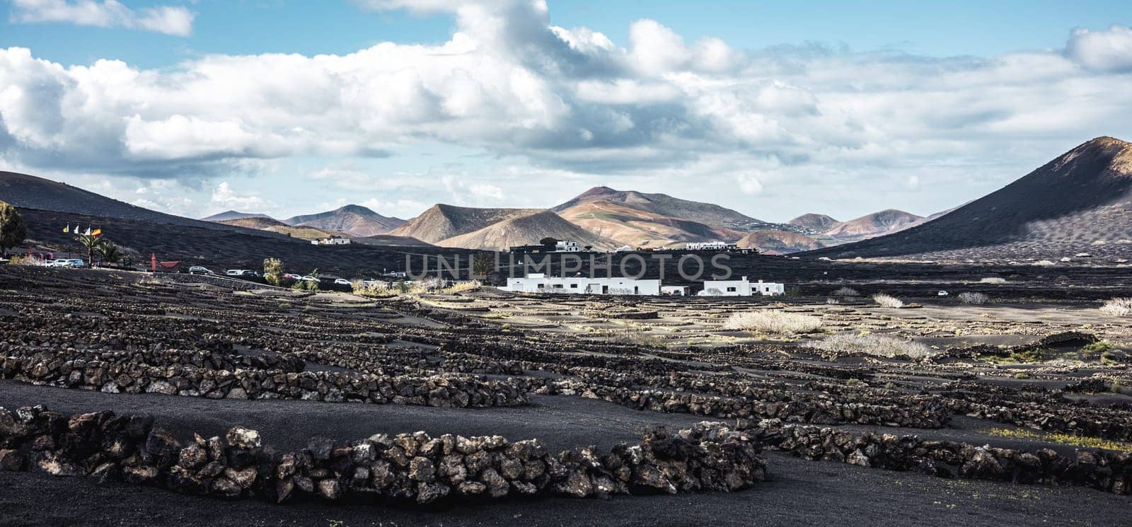 Traditional white houses in black volcanic landscape of La Geria wine growing region with view of Timanfaya National Park in Lanzarote. Touristic attraction in Lanzarote island, Canary Islands, Spain