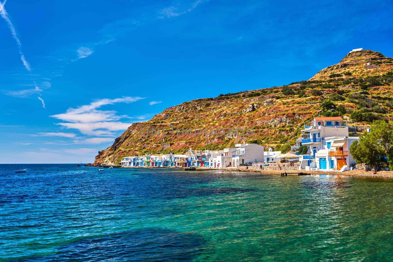 Colorful village of Klima with Greek whitewashed houses on sunny day, Milos island, Cyclades, Greece. Traditional fishermen village, bright painted and weathered doors and doorways, high hill, great blue sky, azure sea, summer sunshine, vacations.