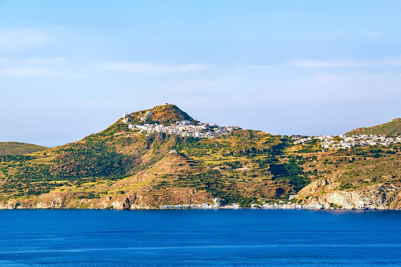 Beautiful view of Mediterranean island and its seashore. Whitewashed houses atop of high hills, terraced slopes and winding roads, white Orthodox churches dominate skyline. Milos, Cyclades, Greece.