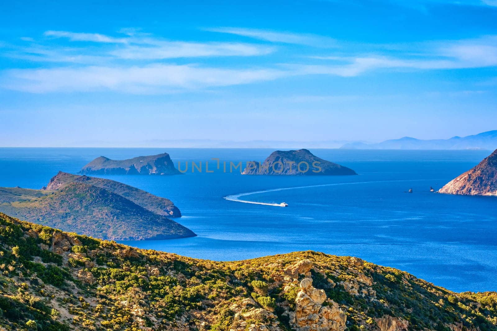 Beautiful landscape with several islets in bay, distant hazy shores, blue sea waters, great sky, sunny summer day in Mediterranean sea. Small ferry speedboat enter picturesque harbour, perfect Greek travel and vacation. Milos island, Greece.