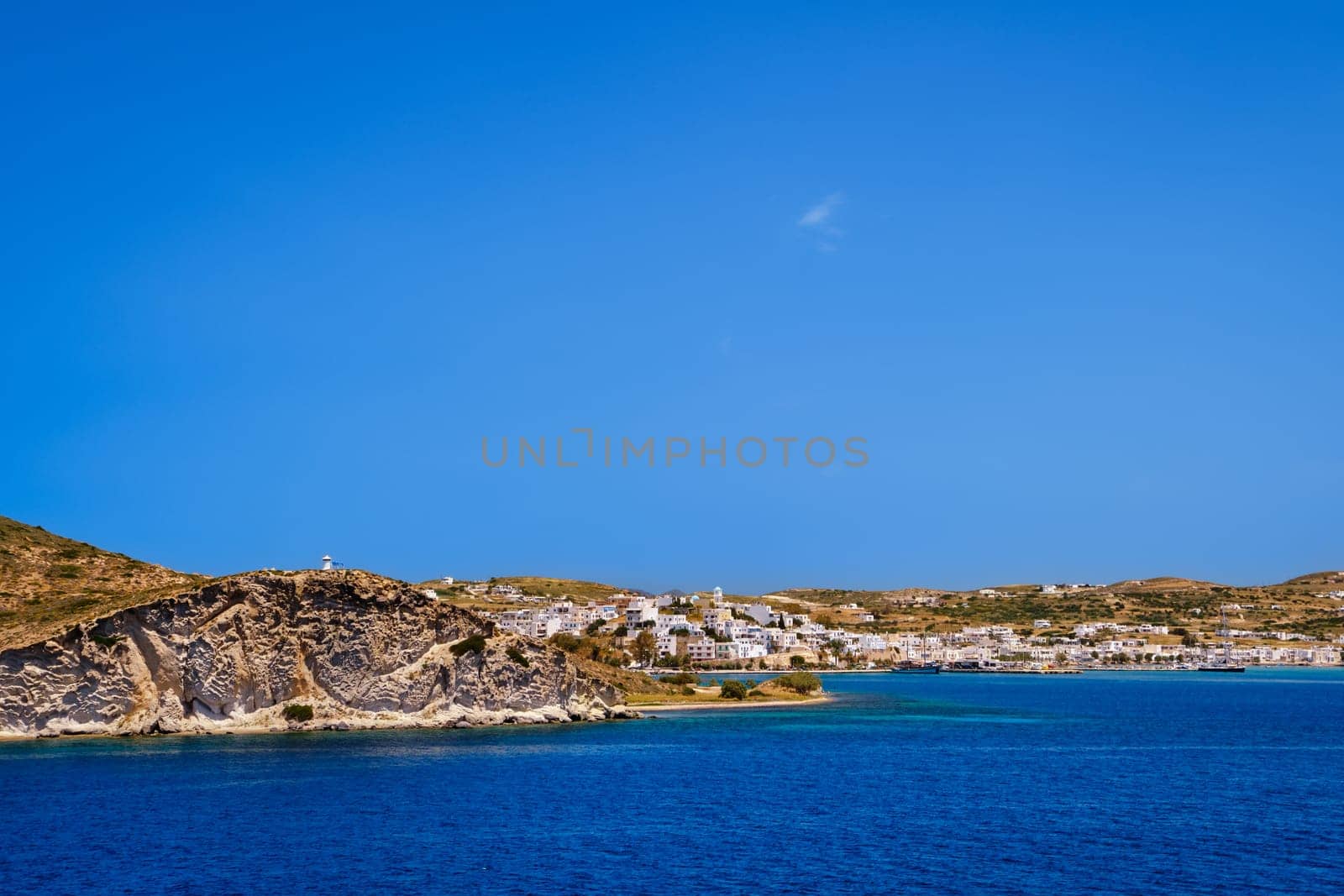 Beautiful summer day and sunshine in typical port town of Greek island. Whitewashed houses on hills and by waterfront. Mediterranean lifestyle, vacations, island hopping, crueses. Milos, Cyclades, Greece.