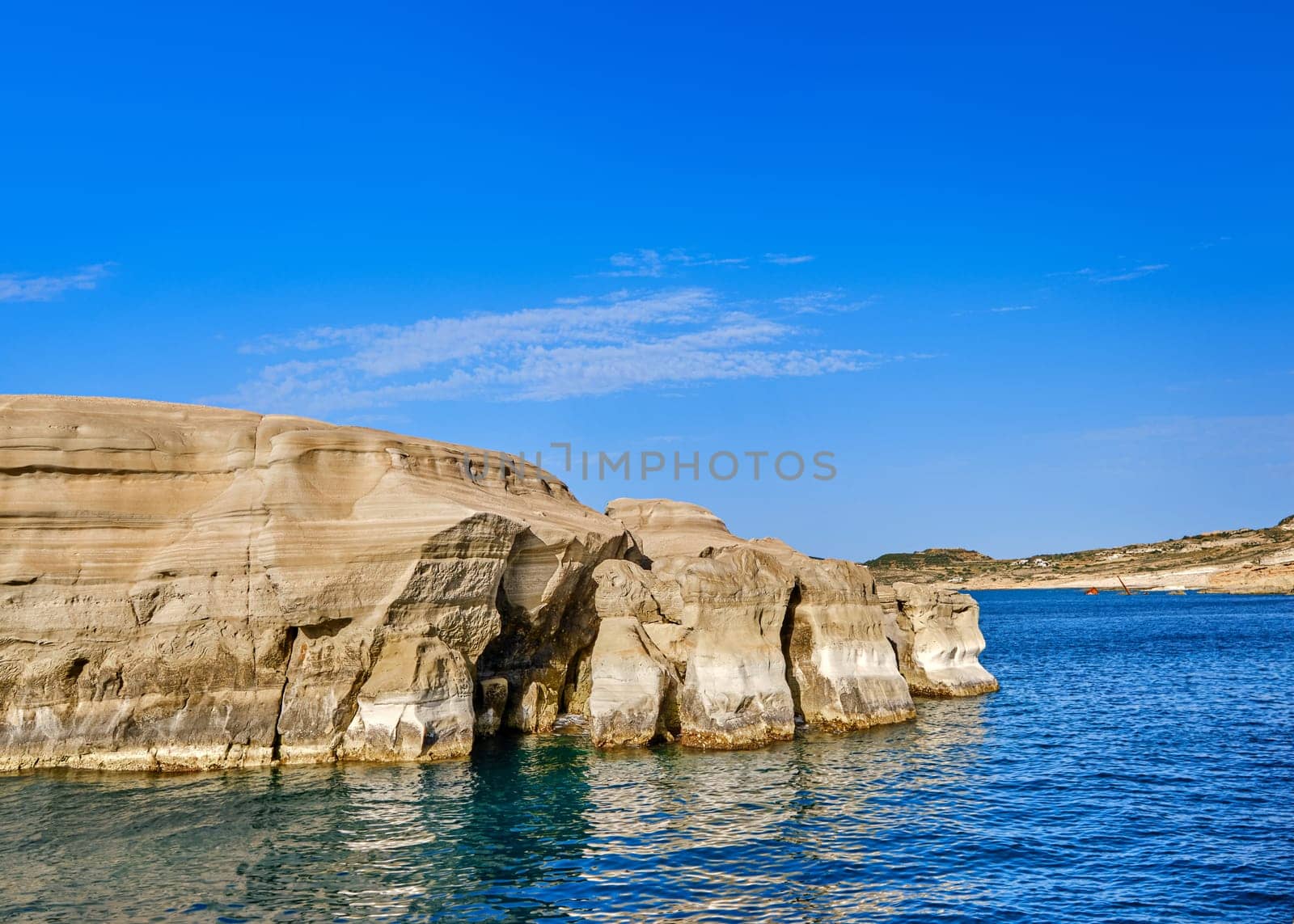 Beautiful view of high hill slope of island in Mediterranean Sea. Blue sea waters, clear blue sky, bright sunshine, summer day, rocks and islets of Aegean sea.