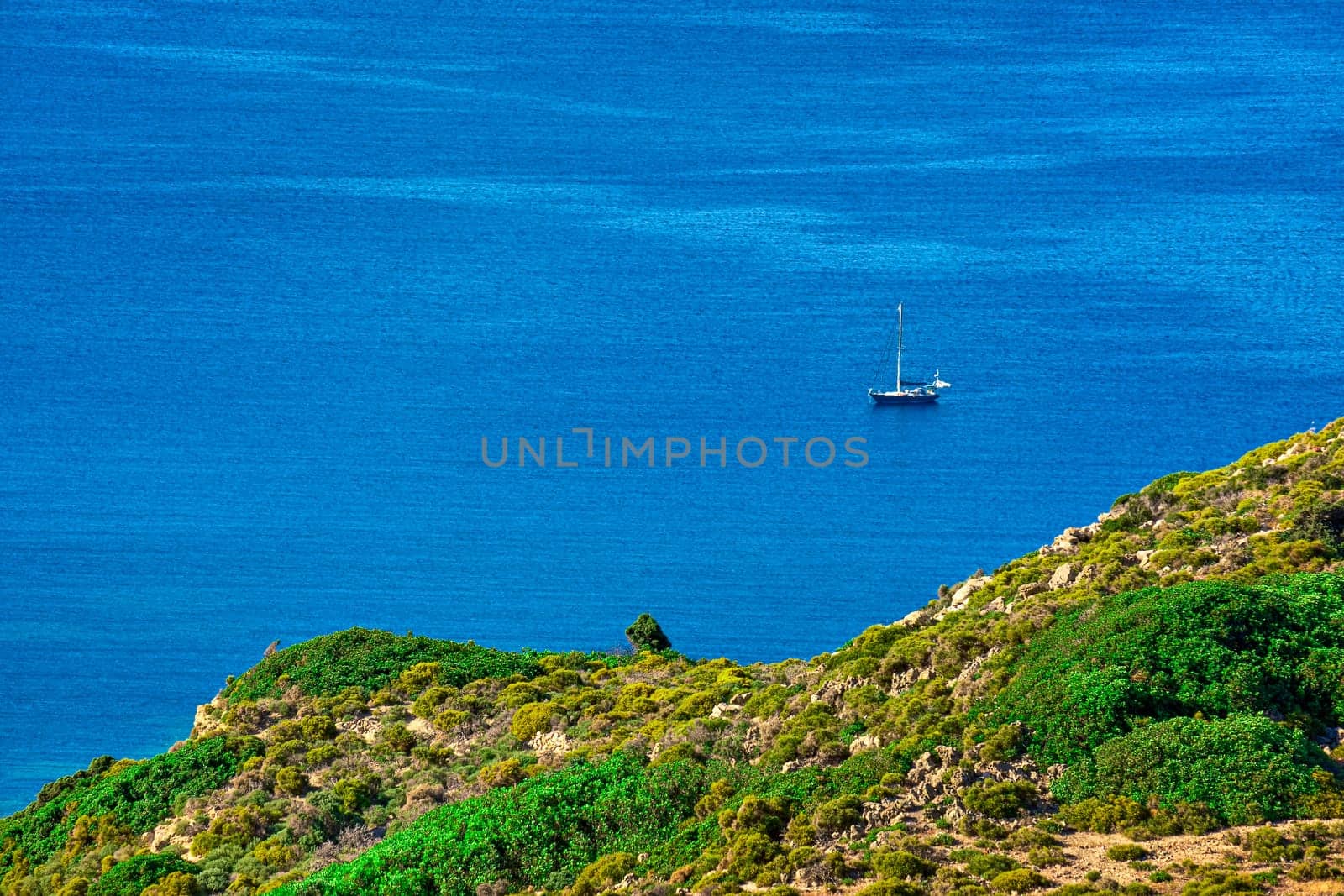 Single sailboat in calm blue sea and green hill in foregrounds, aerial shot. Summer vacations, hiking, sailing, adventure, getaway. Milos, Greece