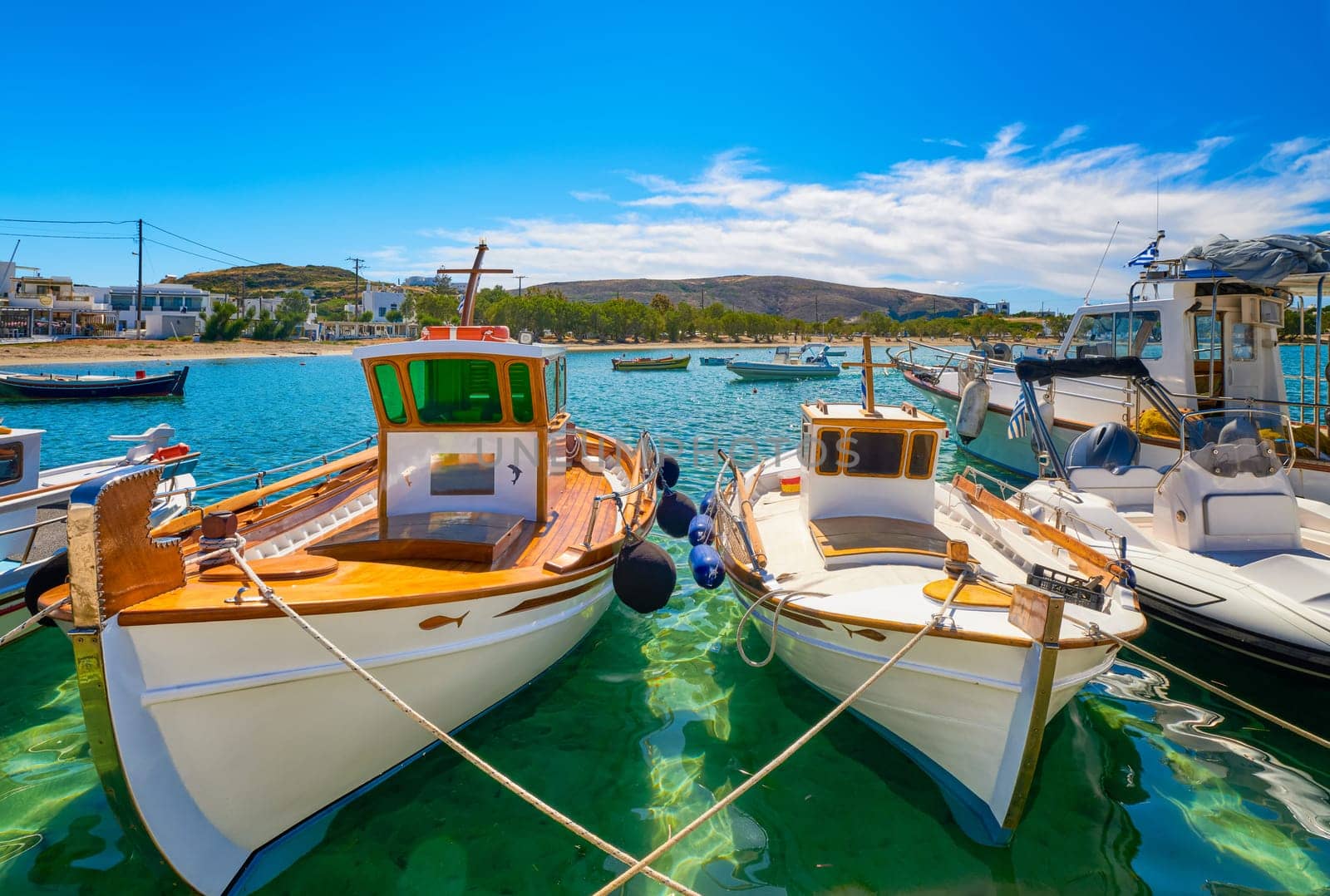 Beautiful view of Greek fishing boats anchored in a small village. Summer day sunshine, island, village, town, whitewashed houses, colorful fishing boats, Mediterranean lifestyle, green hills, vacations, relax, travel destinations. Milos, Greece.
