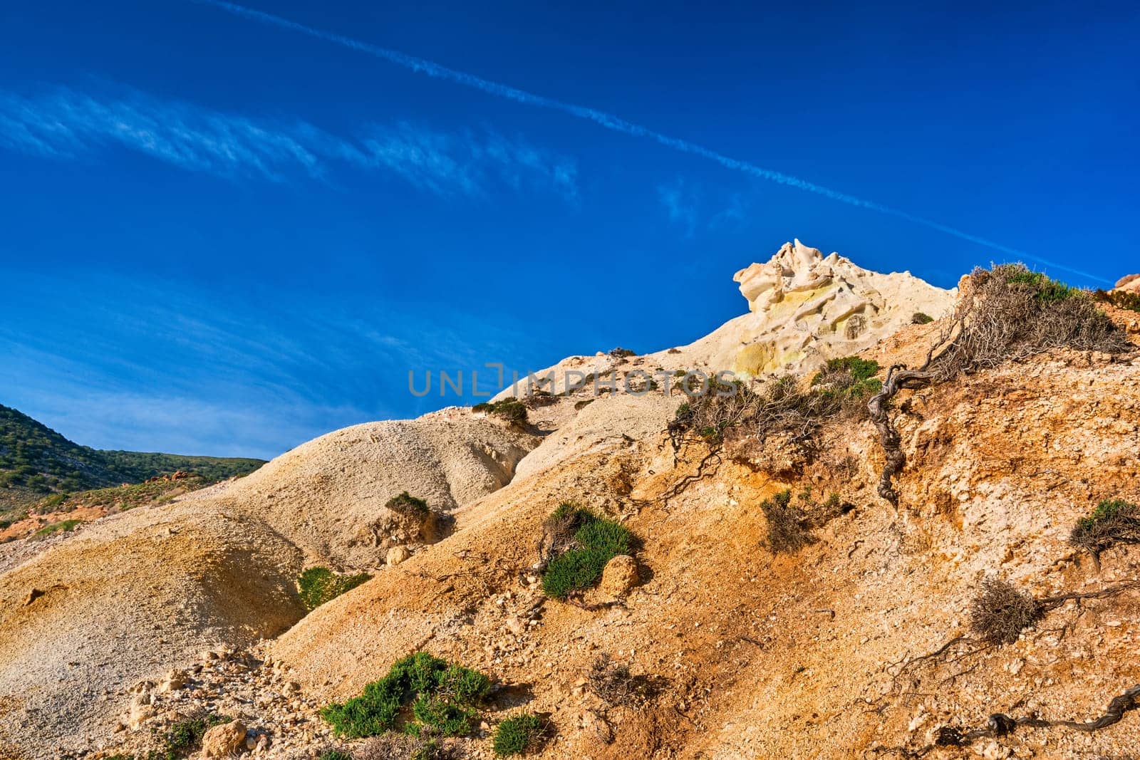 Unique natural rock formations of yellow and orange cliffs in low sunlight, Milos, Greece. Weather-shaped slopes of rocks on Agios Ioannis beach at clear blue sky.