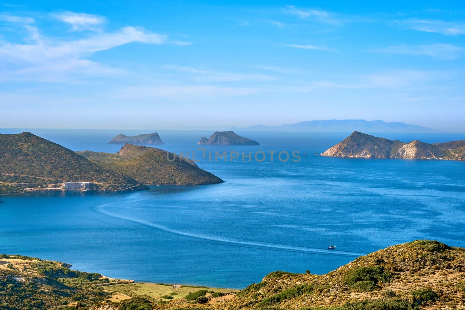 Beautiful landscape with several islets in bay, distant hazy shores, blue sea waters, great sky, sunny summer day in Mediterranean sea. Picturesque harbour, perfect Greek travel and vacation. Milos island, Greece.
