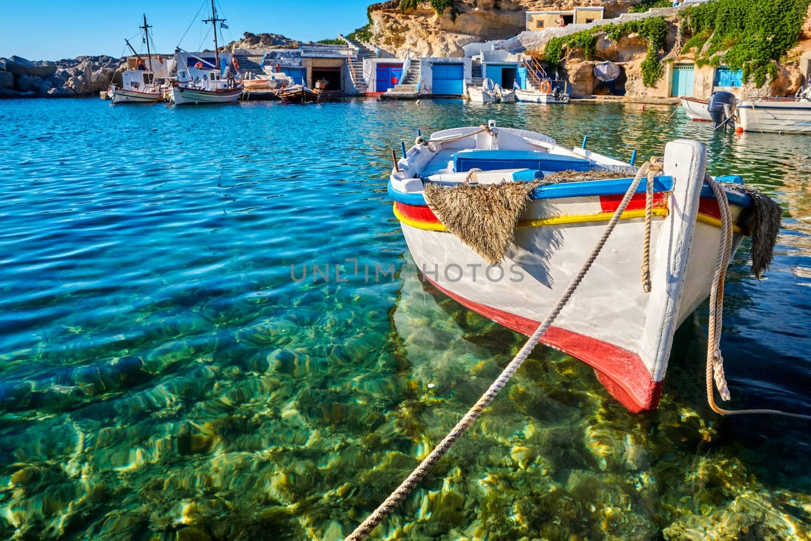 Colorful authentic Greek fishing boats anchored in a small village in crystal clear sea waters. Summer day sunshine, island, whitewashed boat houses, Mediterranean vacations, travel destinations. Selective focus, blurred background. Milos, Greece.