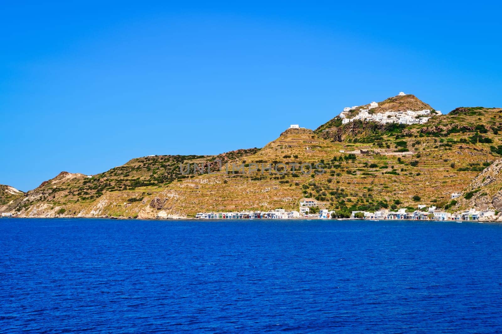 Beautiful summer day and sunshine in typical hill top town of a Greek island. Whitewashed houses on hills and by waterfront. Mediterranean lifestyle, vacations, island hopping, crueses. Milos, Cyclades, Greece.