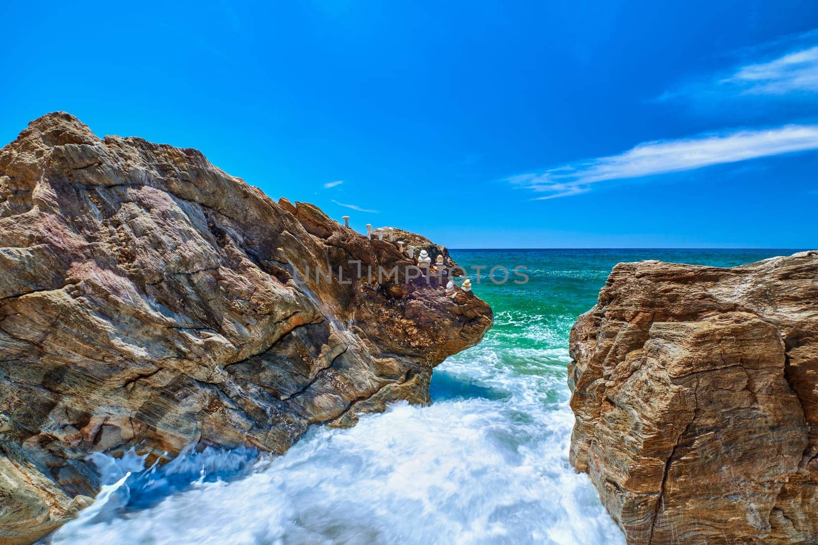 Sea waves beat in rocks on sunny summer day, clear sky, long exposure. Tiny balance stone stack on edge of rock. Azure waters, white sea spray. Perfect seascape, vacations destination. Paleochori beach, Milos, Greece