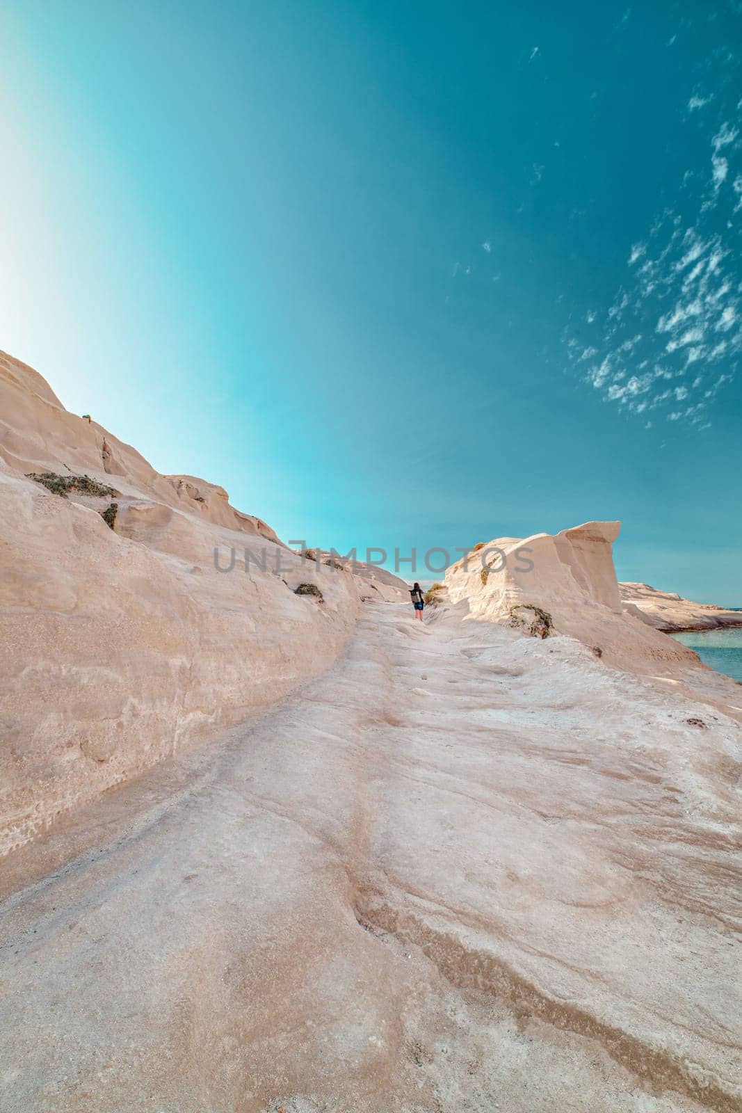 Beautiful white rocks of Sarakiniko beach, Aegean sea, Milos island , Greece. Lonely unrecognizable adult, empty cliffs, summer day sunshine, lunar landscape, fantastic rocks of tourist destination, sky, clouds, cyan-pink colors, vertical shot