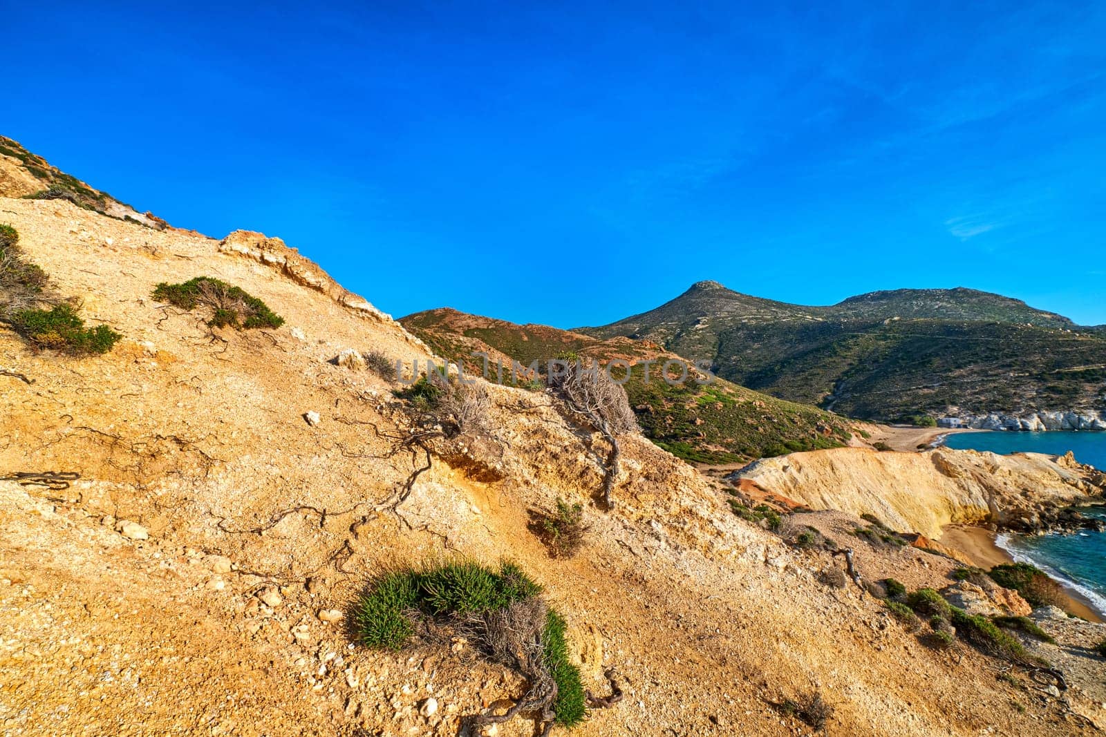Unique natural rock formations of yellow and orange cliffs in low sunlight, Milos, Greece. Weather-shaped slopes of rocks on Agios Ioannis beach at clear blue sky.