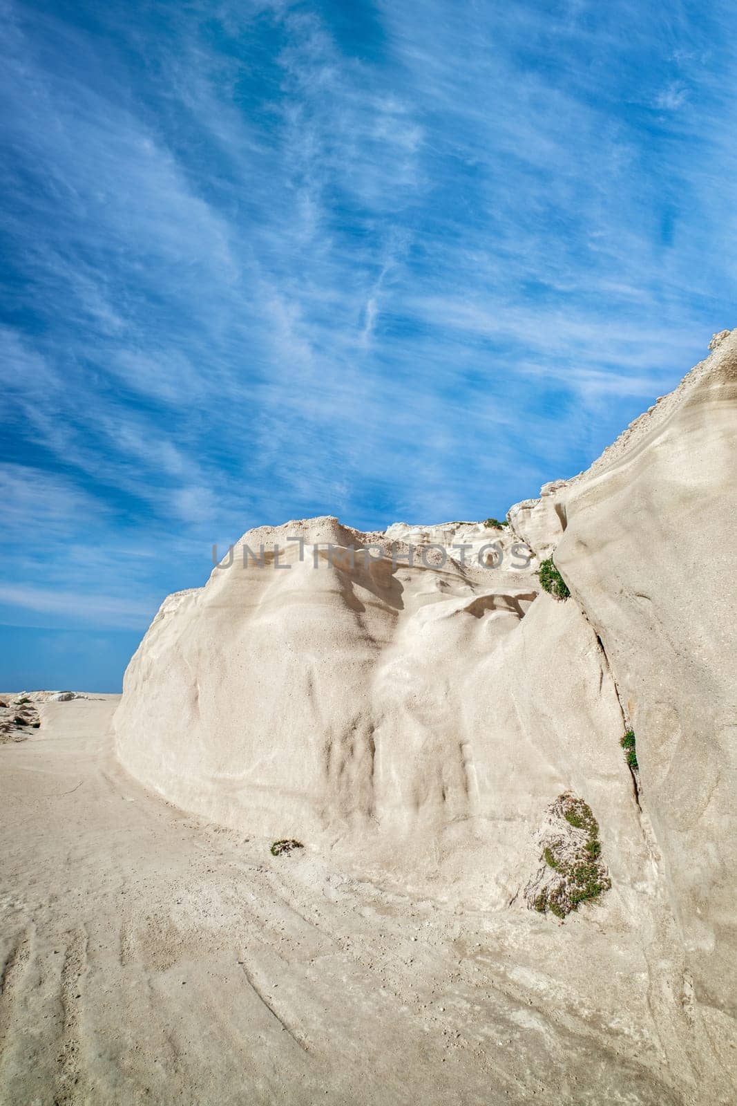 Beautiful white rocks of Sarakiniko beach, Aegean sea, Milos island , Greece. No people, empty cliffs, summer day sunshine, lunar landscape, fantastic rocks of tourist destination, deep blue sky, clouds, vertical shot