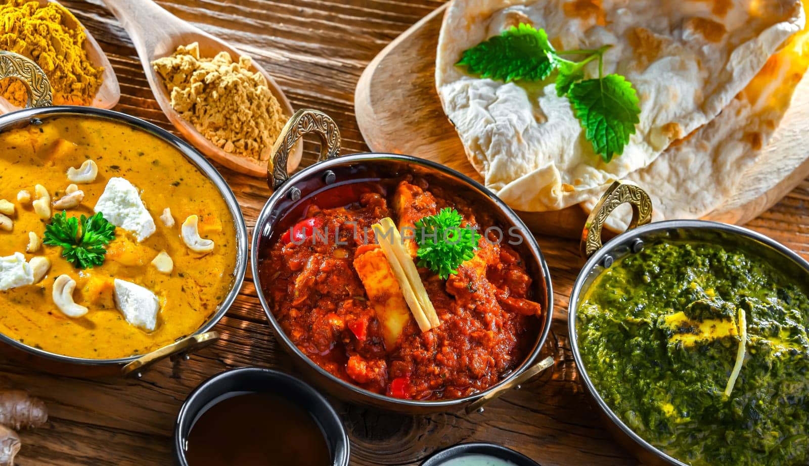 Composition with indian dishes: madras paneer, palak paneer and shahi paneer with basmati rice served in original indian karahi pots.