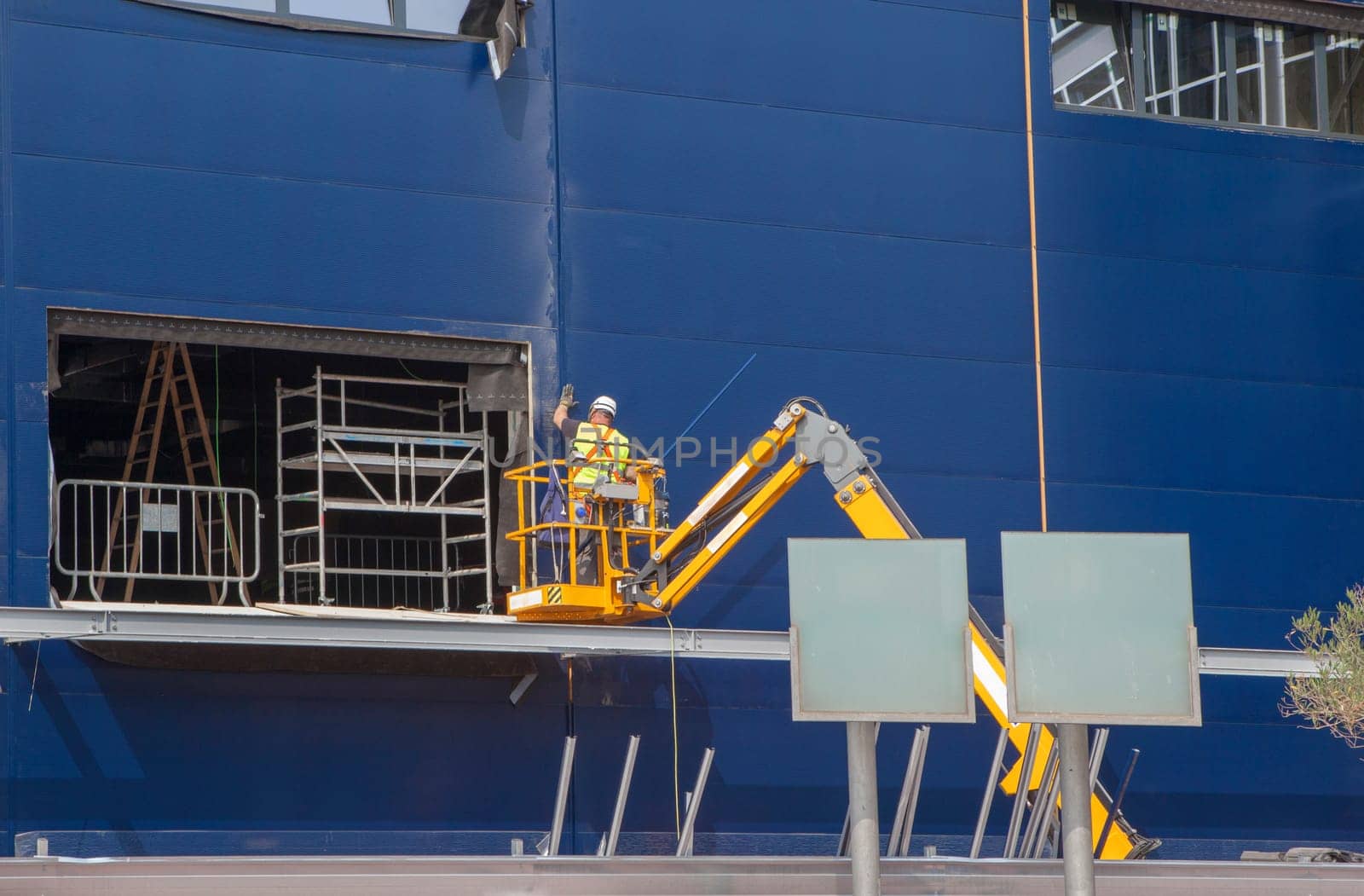 Worker installing insulating panels in a building under construction. He is over telehander crane
