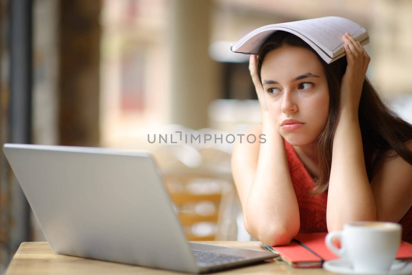 Frustrated student distracting looking away sitting in a bar terrace