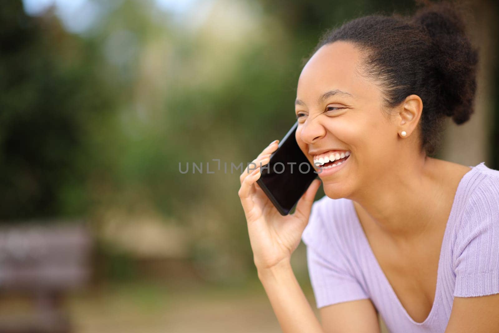 Happy black woman talking on phone laughing in a park