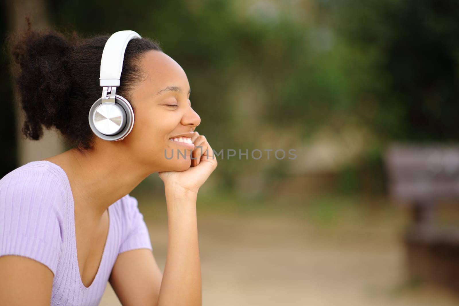 Happy black woman relaxing listening audio with headphone and closed eyes in a park