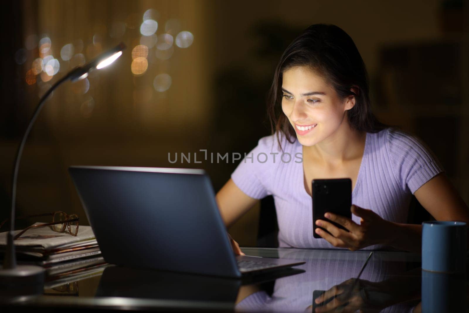 Happy woman using several devices cheking laptop in the night at home