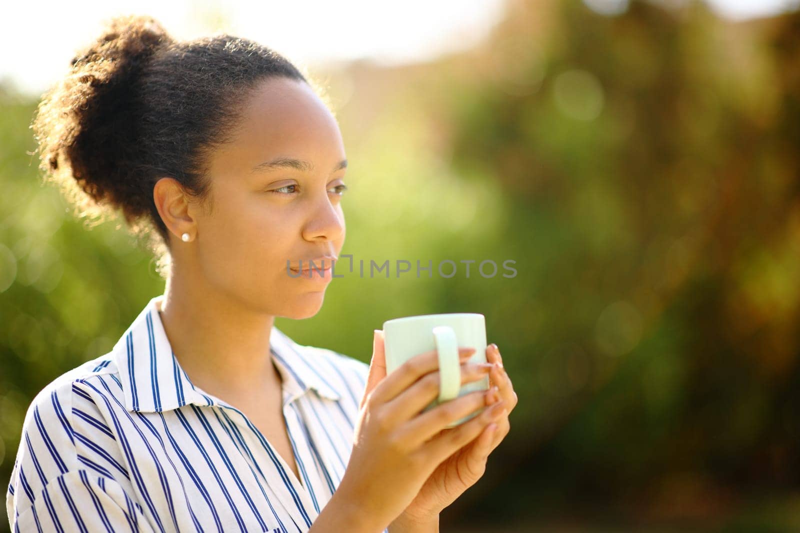 Relaxed black woman holding coffee mug looks away in a park