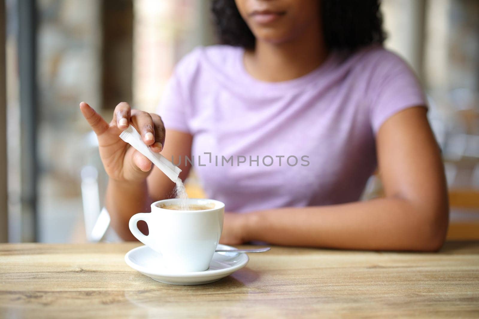 Close up of a black woman throwing sugar in a coffee cup in a bar terrace