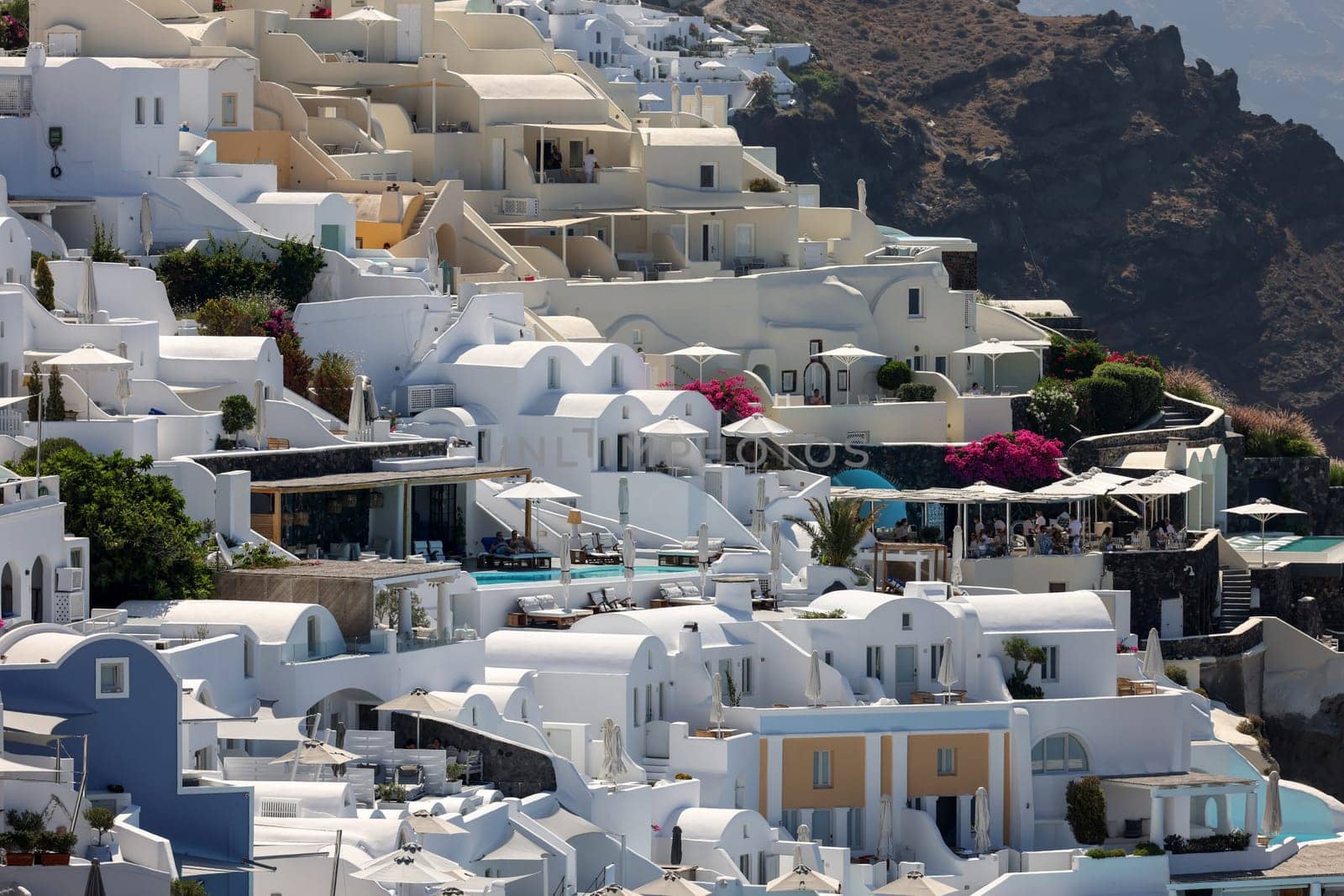 Oia, Santorini, Greece - July 3, 2021: Whitewashed houses with terraces and pools and a beautiful view in Oia on Santorini island, Greece