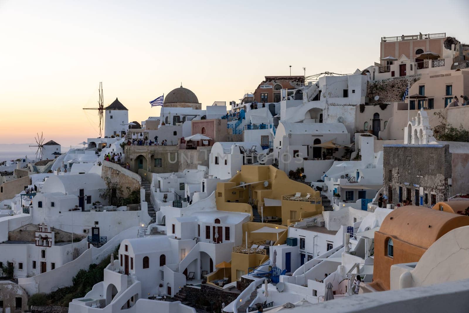 Oia, Santorini, Greece - June 28, 2021: Whitewashed houses and windmills in Oia in warm rays of sunset on Santorini island. Greece