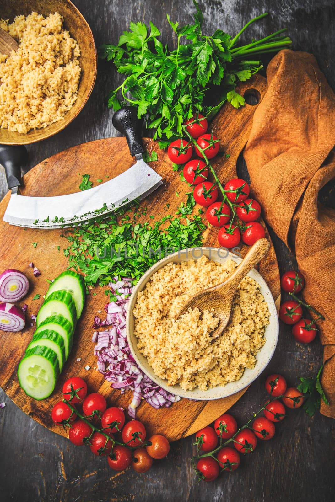 Preparing traditional oriental salad Tabouleh with couscous or bulgur, ingredients on cutting board