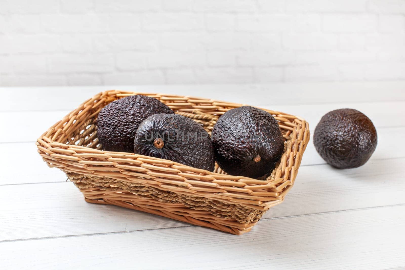 Dark brown avocados ( bilse variety ) in square wooden basket on white boards desk.