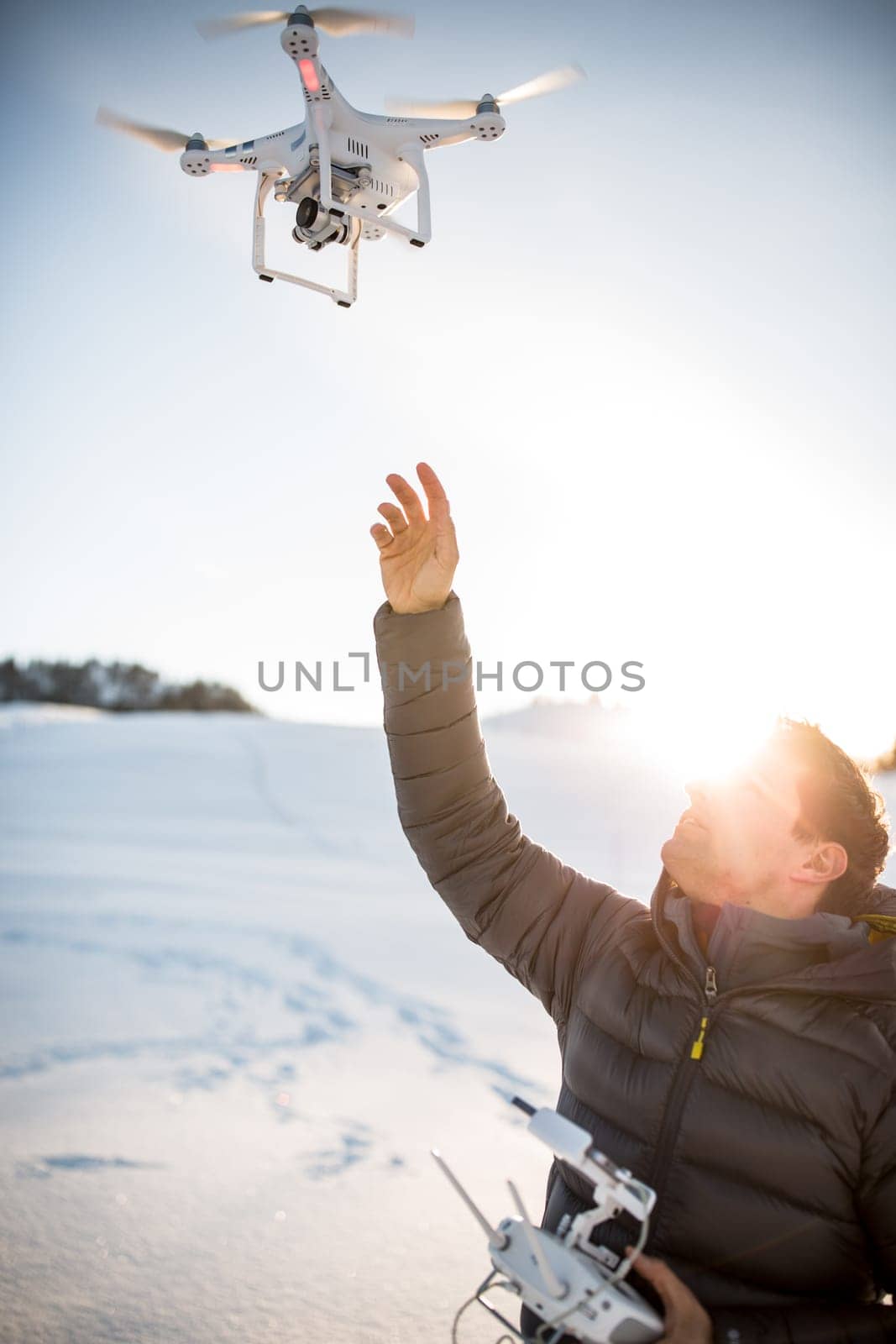 Young man controlling his drone in snowy outdoors. Drone operator holding a transmitter and landing with a drone.