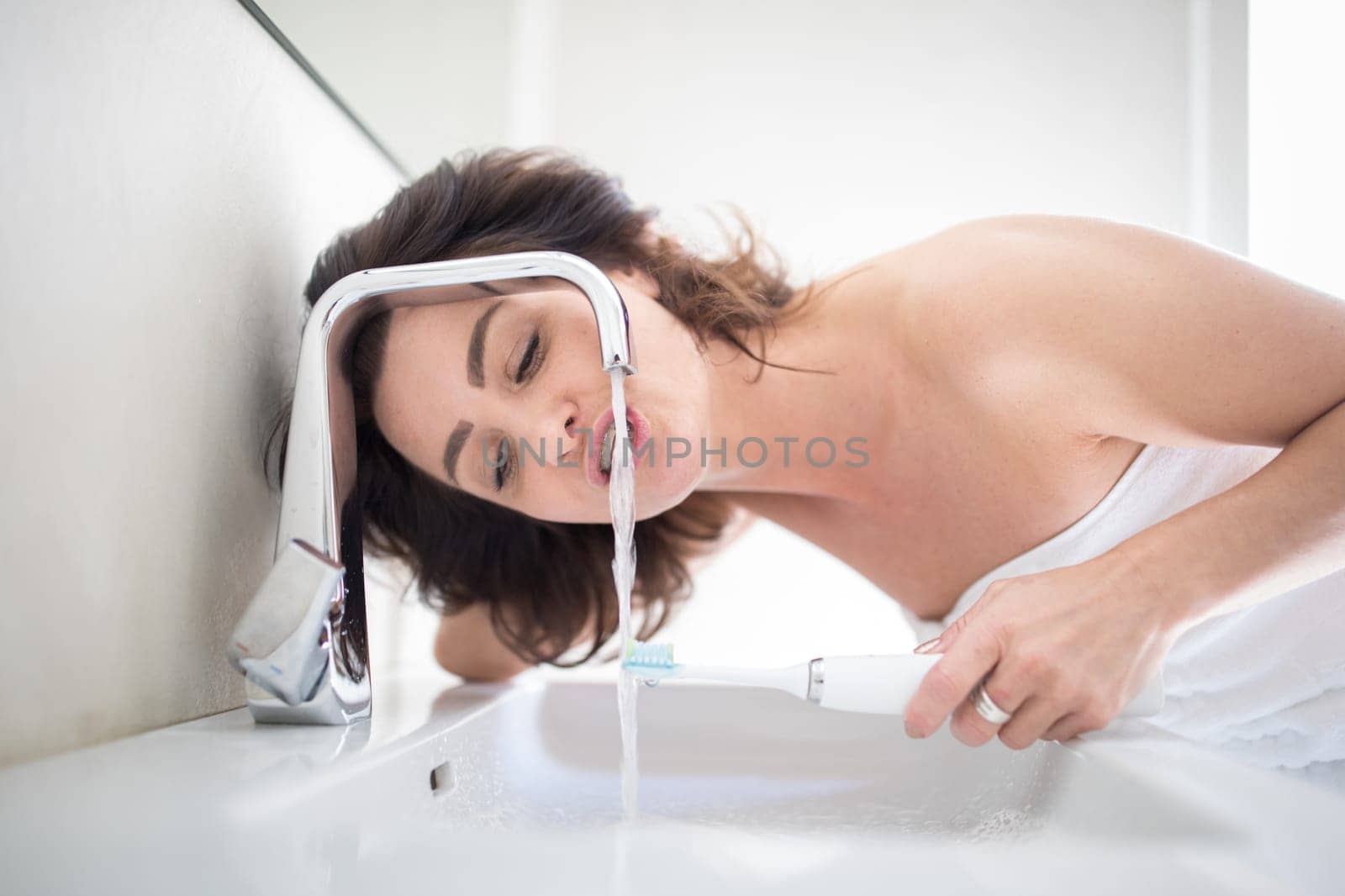 Pretty, middle aged woman brushing her teeth in a modern design bathroom