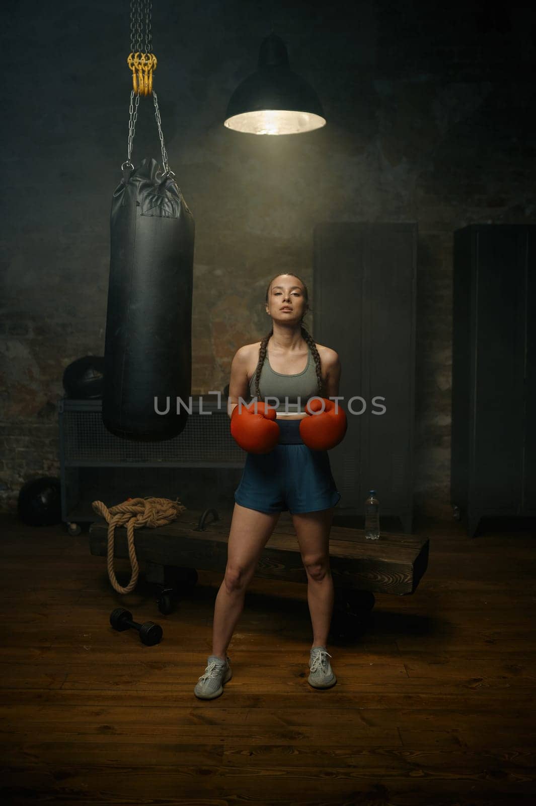 Portrait of beautiful sportive woman in red boxing gloves posing in gym studio