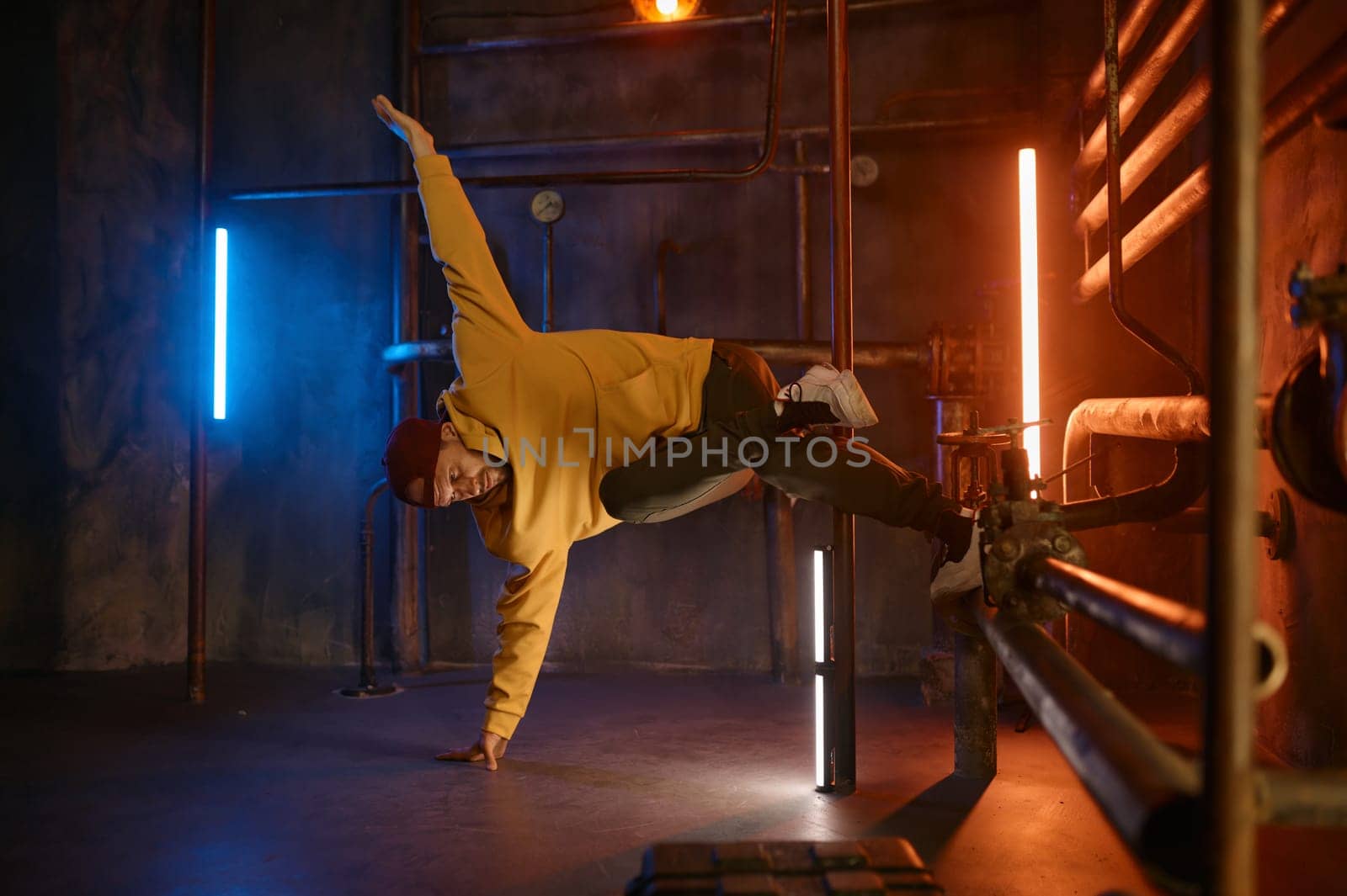 Modern hip hop dancer frozen in movie standing on one hand holding steel pilon tube practicing in dance over urban subway station background