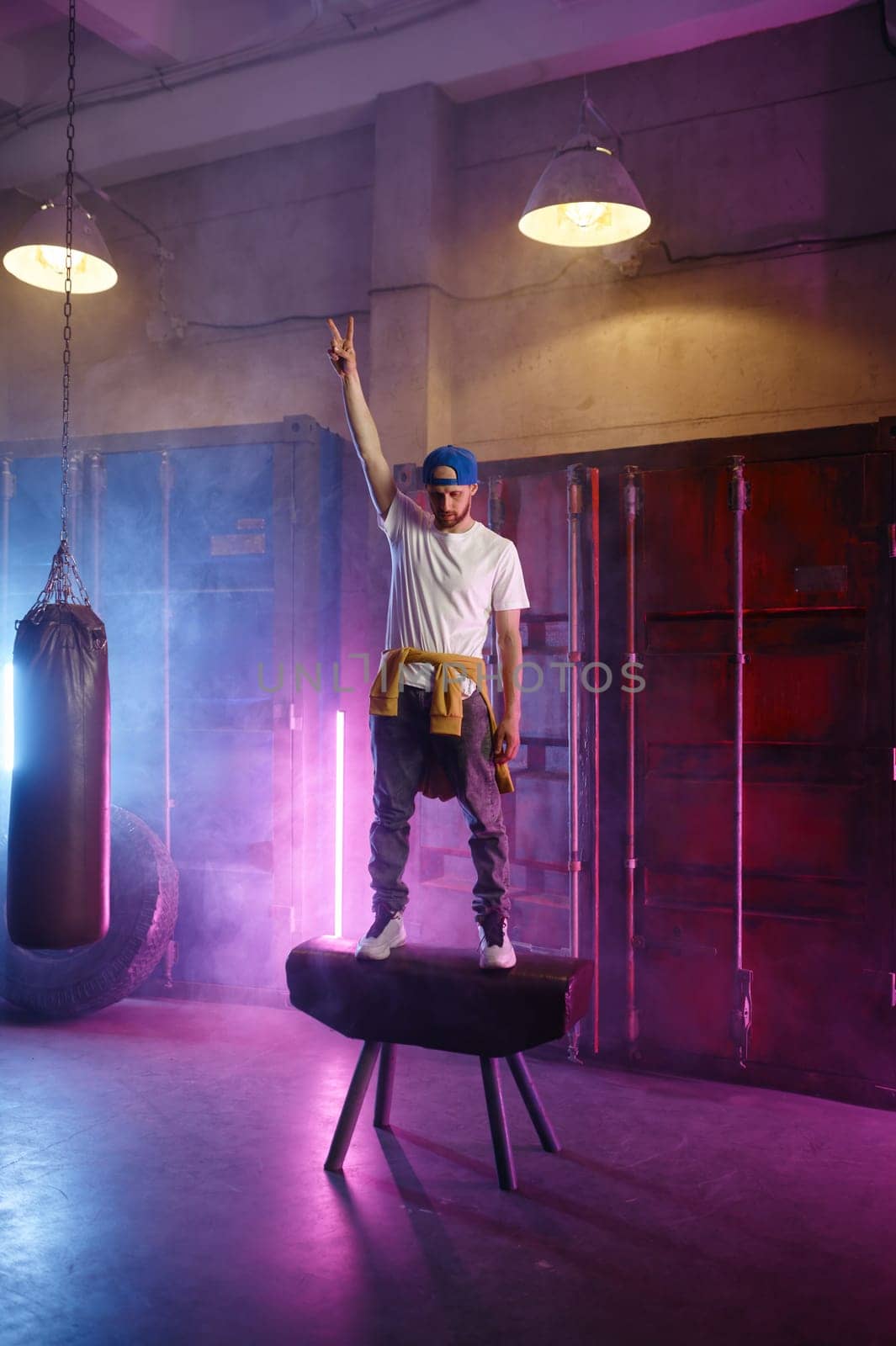 Cool hip hop dancer in trendy street clothes standing on sports gymnastic apparatus preparing to make trick jump. Breakdance freestyle performance concept