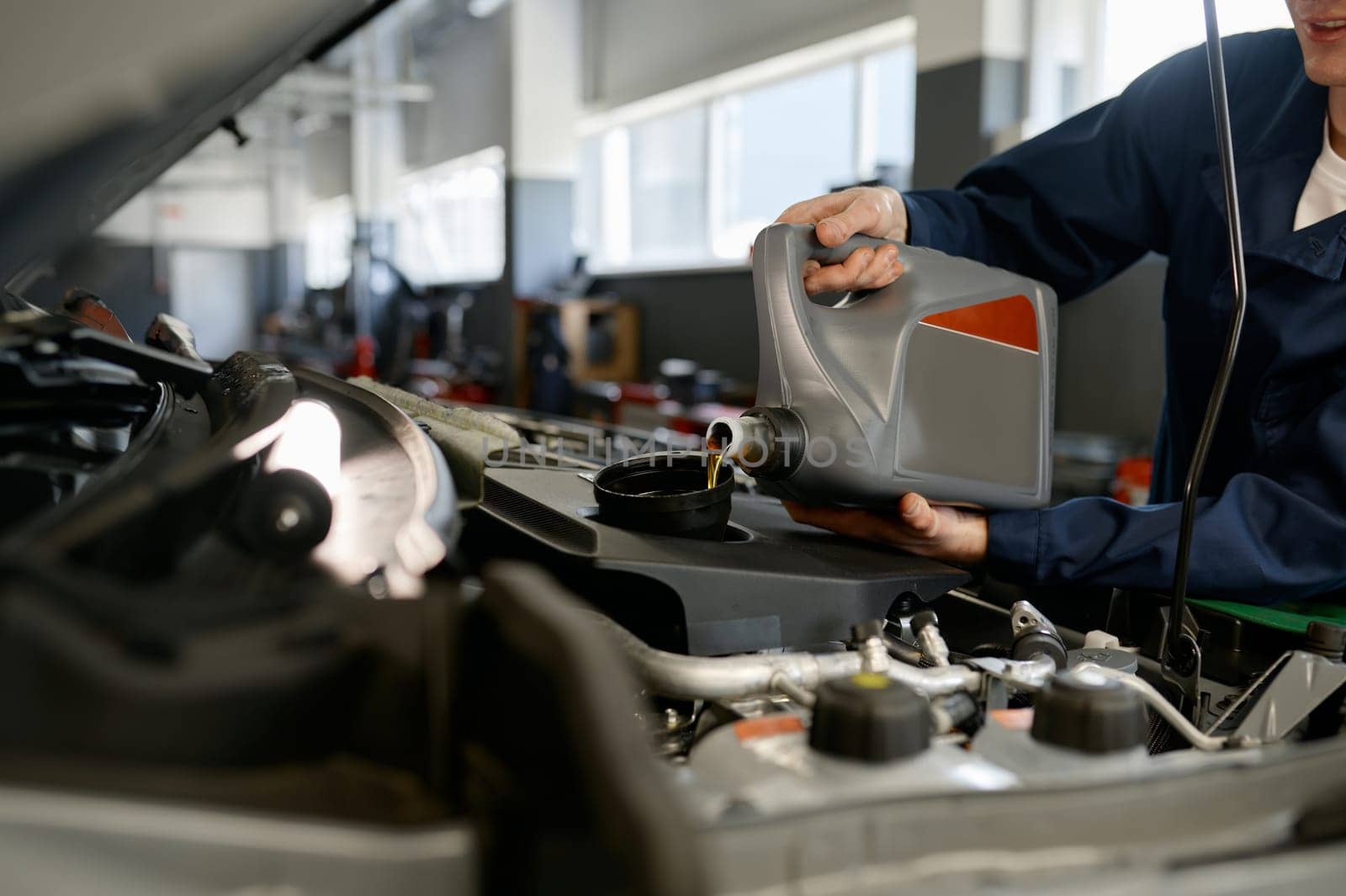 Closeup of mechanic pouring fresh oil into car engine from plastic container. Automobile maintenance and repair service station
