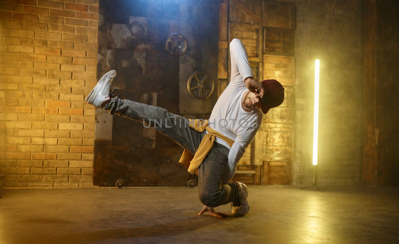 Young man breakdancer. Active stylish guy hip hop dancer training or performing over loft studio background