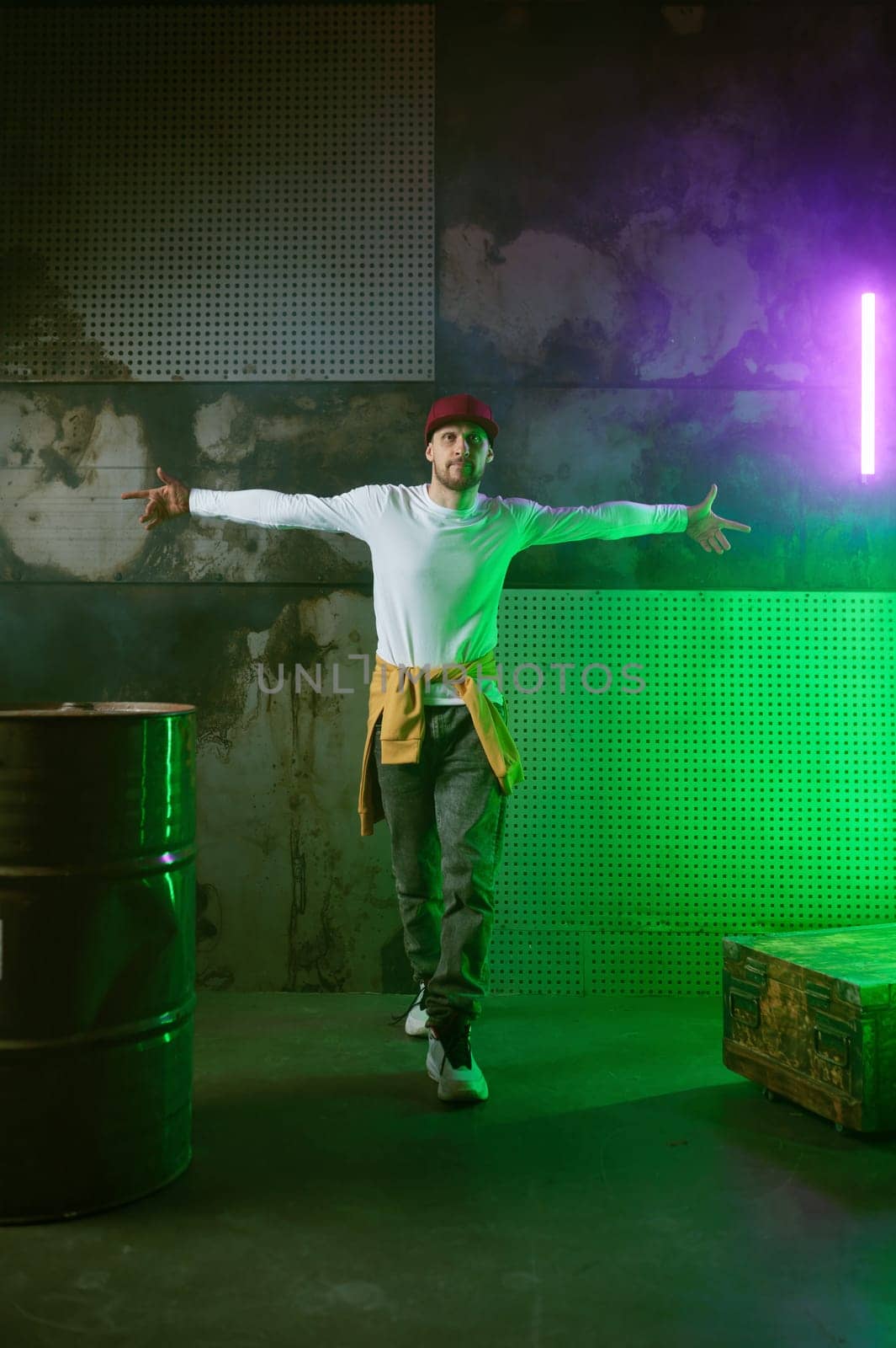 Male break dancer performing on loft stage in green neon light. Professional stylish guy breakdancer acrobat making tricks in expressive dance