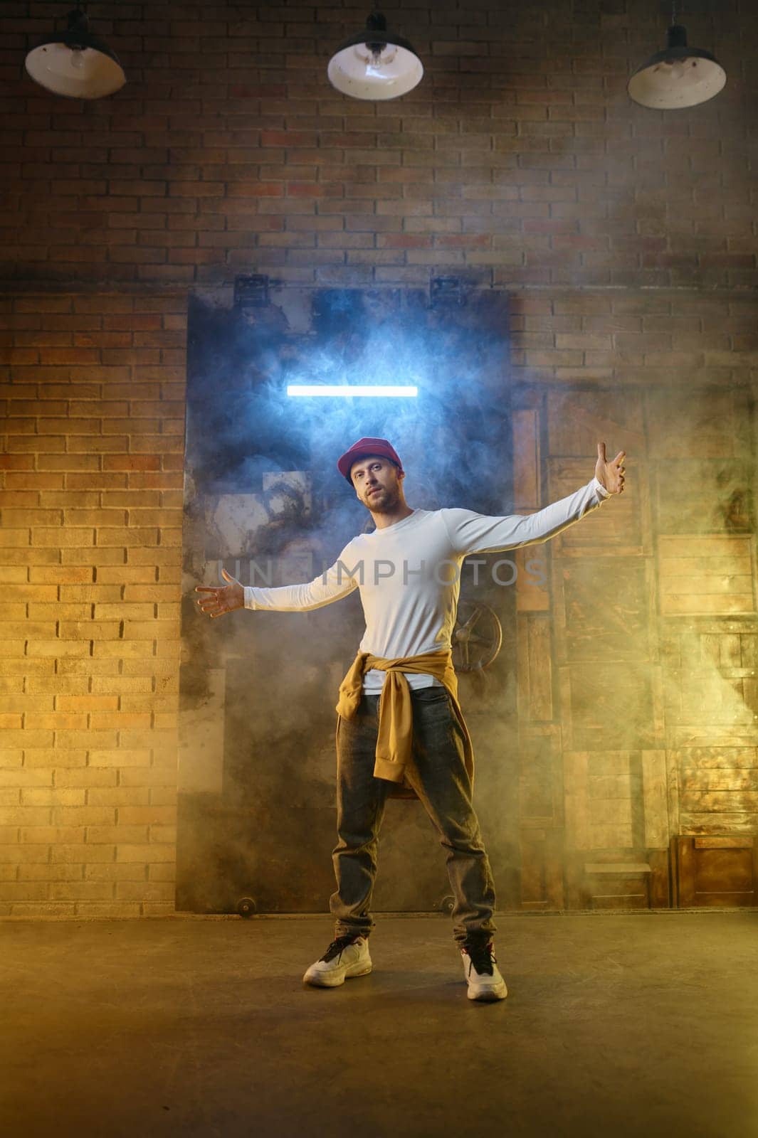 Contemporary hip hop freestyle dancer posing for camera standing in cool position gesturing with wide spread arms get ready for dance challenge competition