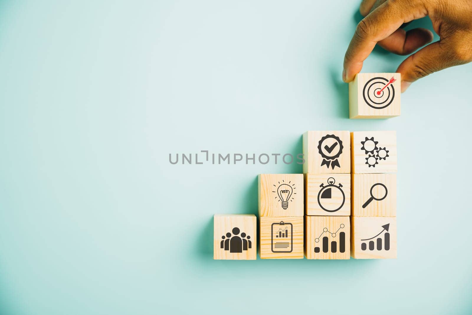 Hand arranging wood block stacking to depict the business strategy and action plan on blue background. Showcasing the concept of business development and targeting business goals. Copy space included