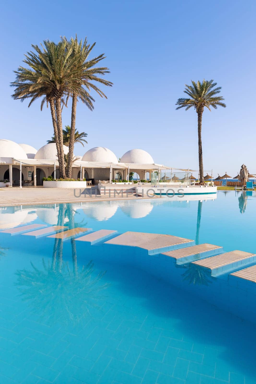 Swimming pool and palm trees with traditional building with dome roof, Tunisia
