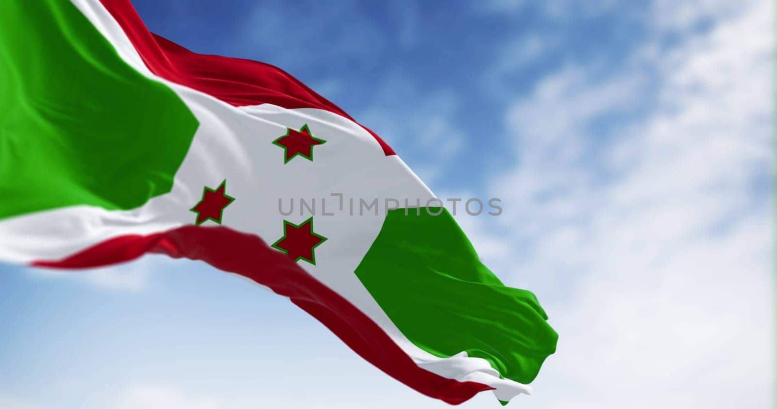 National flag of Burundi waving on a clear day. White diagonal cross dividing into red and green sections, three green stars in the center. 3d illustration render. Fluttering fabric. Selective focus