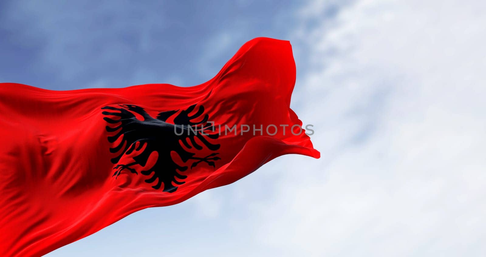 Albanian national flag waving in the wind on a clear day. Red flag with black two-headed eagle. 3d illustration render. Fluttering fabric.
