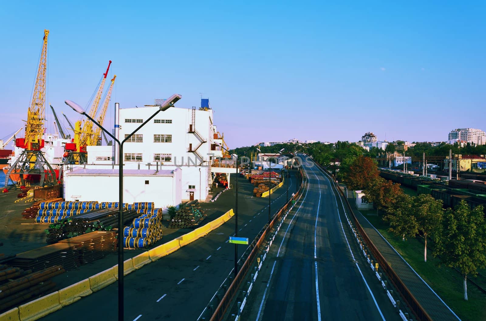 The road from seaport to the city, port cranes railway cars, city buildings on a background.