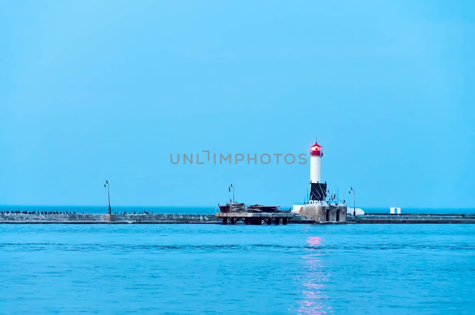 Illuminated lighthouse in twilight, light beam shines in dark skies 