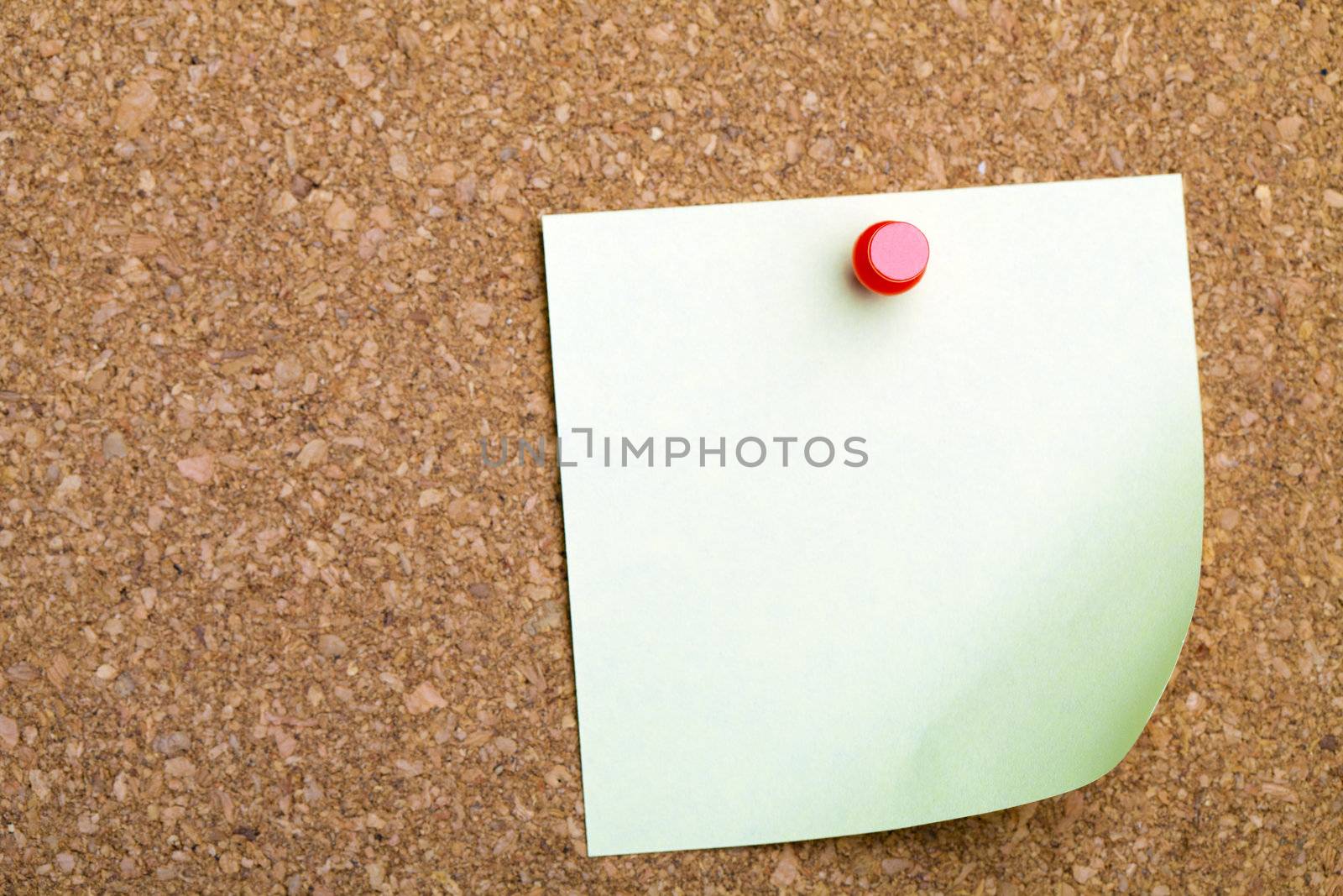 A sticky note with a curled up corner on a corkboard