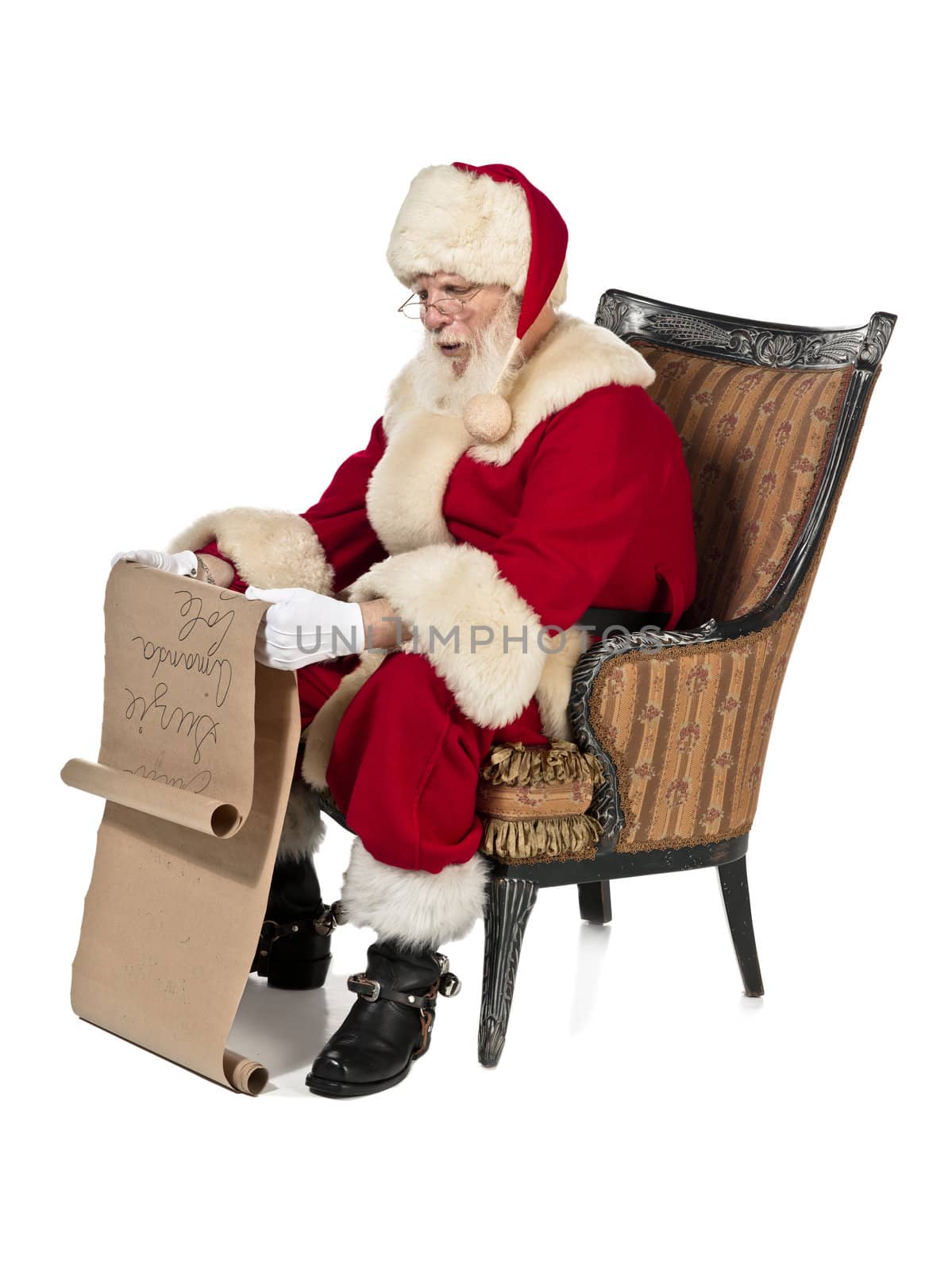 Santa clause reading Christmas wish list wearing a red costume while sitting on a chair 