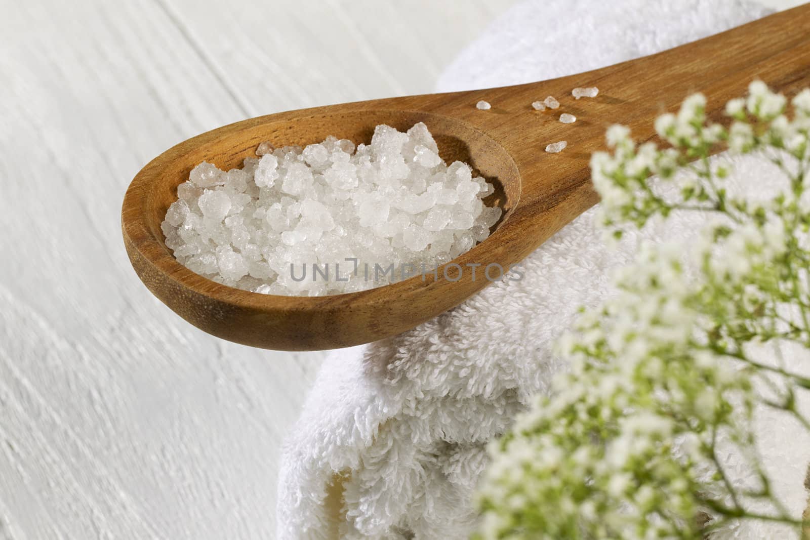 A spoon of spa salt and a white towel on a wooden background 