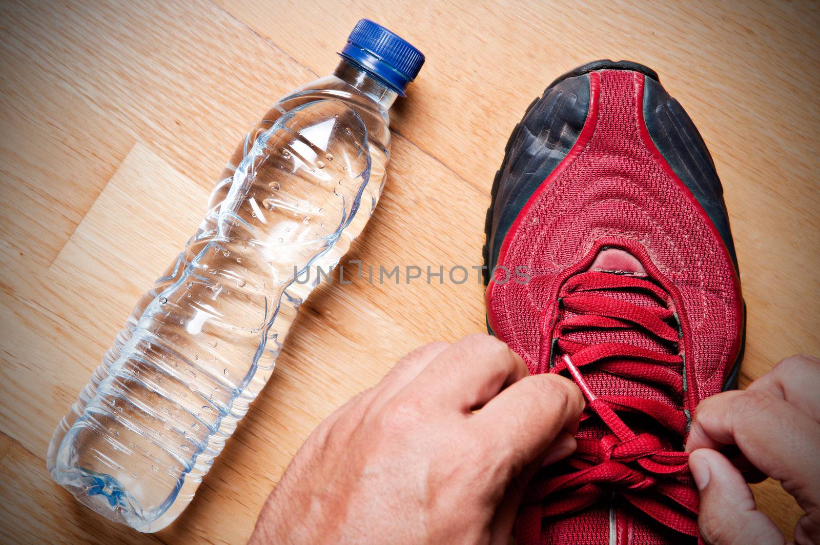 Jogger at home, tying his sneakers with a water bottle nearby